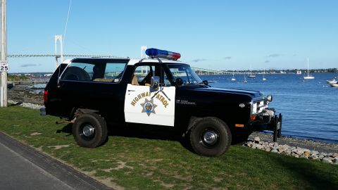 1991 Ford LTD Crown Victoria - A vintage Dodge Ramcharger, marked as Highway Patrol, sits by the water with a bridge and sailboats in the distance.
