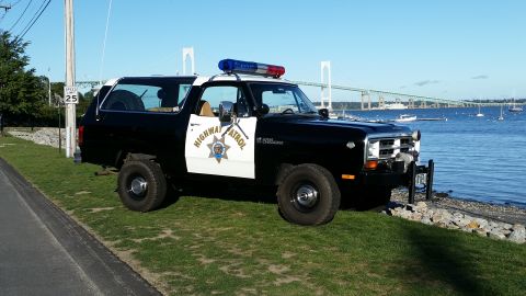 1991 Ford LTD Crown Victoria - This highway patrol SUV, likely from the 1980s, is parked near the water with a bridge visible in the distance.