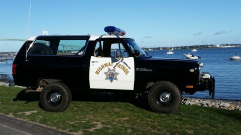 1991 Ford LTD Crown Victoria - This Dodge Ramcharger police vehicle is parked by the water with boats in the background.