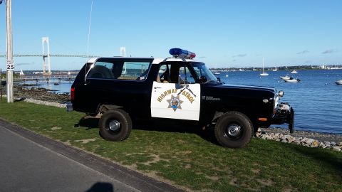 1991 Ford LTD Crown Victoria - This highway patrol SUV is parked on a grassy area next to the water, with boats visible in the background.