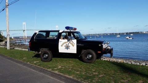 1991 Ford LTD Crown Victoria - A vintage Dodge Ramcharger, marked as Highway Patrol, sits by the water with a bridge and sailboats in the distance.