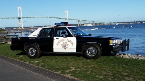 1991 Ford LTD Crown Victoria - A black and white police car with 'Highway Patrol' on the door is parked on a grassy area near the water, with a bridge visible in the dist…