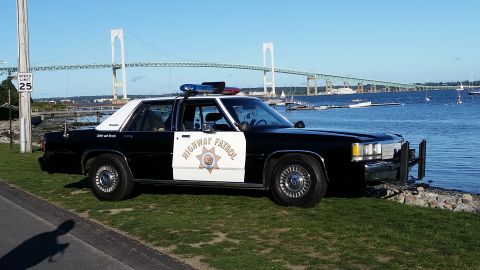 1991 Ford LTD Crown Victoria - A police car with "Highway Patrol" text and emblem is parked by the water, with a large bridge and boats in the background.