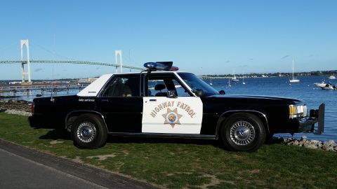 1991 Ford LTD Crown Victoria - Side view of a 1991 Ford Crown Victoria marked as Highway Patrol, parked near a body of water with a bridge visible.