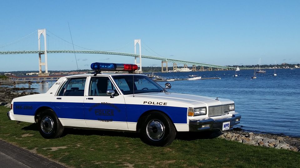 Old police car parked by the water with a bridge in the background