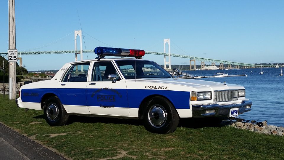 White and blue police car parked by the water with a bridge in the background