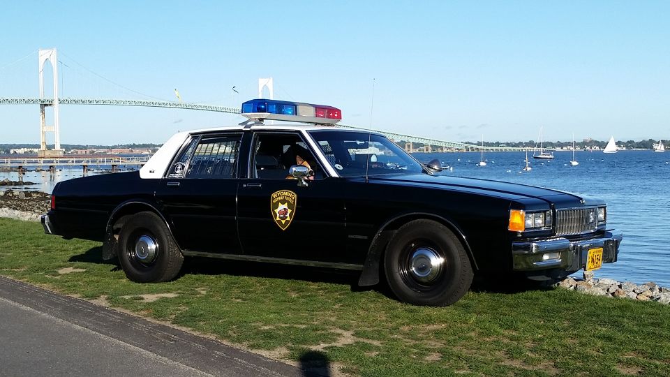 Black police car parked by the water with a bridge in the background