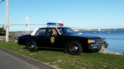 1991 Ford LTD Crown Victoria - Photo of a black and white Chevrolet Caprice police car at a waterfront, not a technical document.