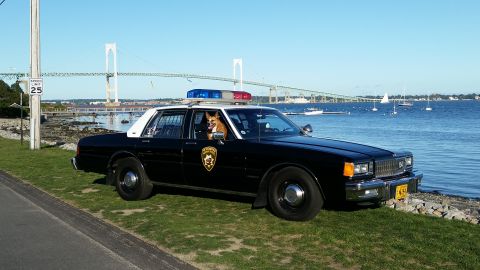 1991 Ford LTD Crown Victoria - Photo of a black and white Chevrolet Caprice police car parked along a bayside road, not a technical document.
