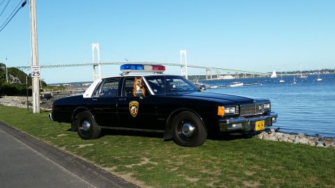 1991 Ford LTD Crown Victoria - Photo of a black and white Chevrolet Caprice police car at a waterfront with a bridge behind, not a technical document.
