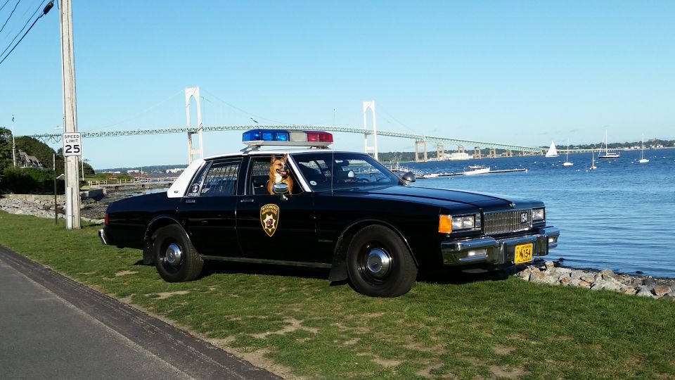 Black and white Chevrolet Caprice police car at a waterfront with a bridge backdrop
