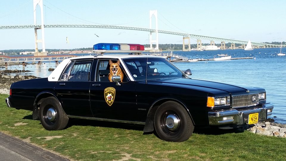 Black and white Caprice police car at the waterfront with a dog and a suspension bridge