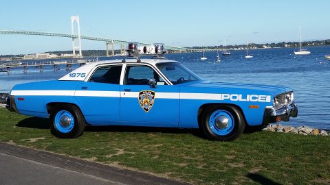 1991 Ford LTD Crown Victoria - Side view of a vintage police car parked near a body of water with a bridge in the background.