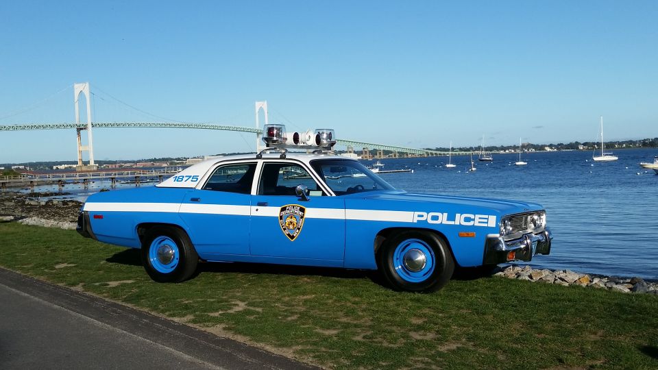 Blue and white police car parked by the water with a bridge in the background