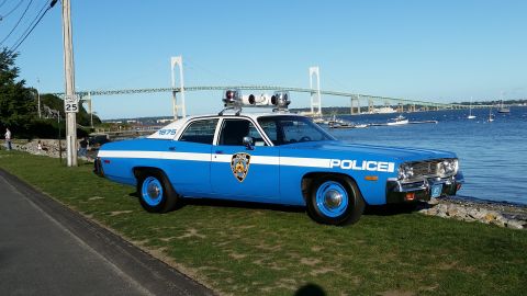 1991 Ford LTD Crown Victoria - Photograph of a vintage blue-and-white NYPD-style police sedan parked near a harbor with a suspension bridge behind.