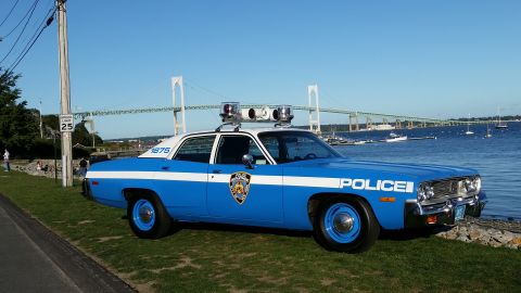 1991 Ford LTD Crown Victoria - Photograph of a restored blue-and-white police sedan with roof lights parked by a harbor and suspension bridge.