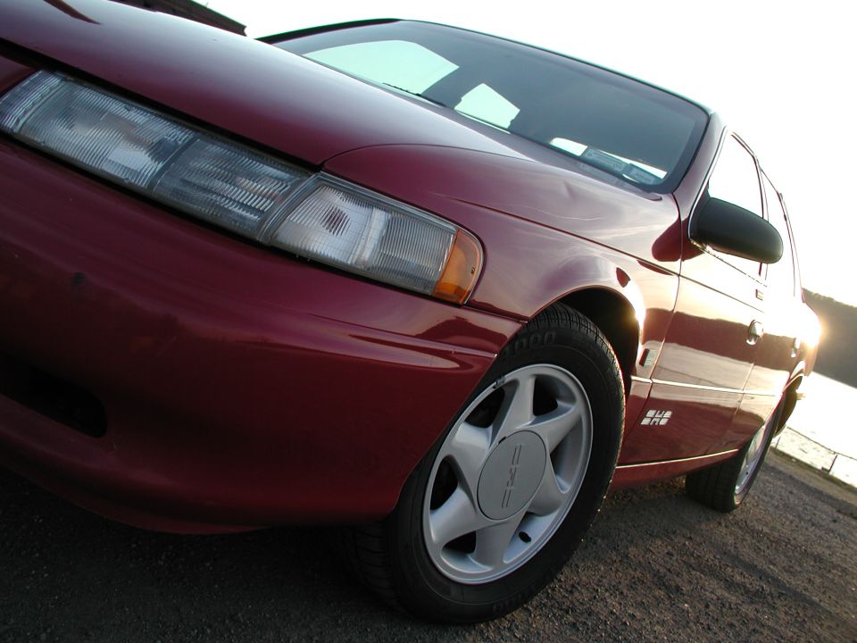 Close-up low angle of a red sedan front corner showing headlight and alloy wheel