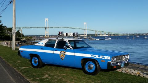 1991 Ford LTD Crown Victoria - Photograph of a vintage blue-and-white police sedan parked at a waterfront with a suspension bridge behind.