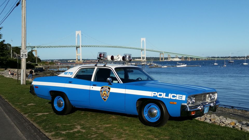 Blue and white vintage police sedan parked on grass near a bridge