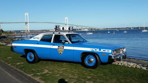1991 Ford LTD Crown Victoria - Photograph of a restored blue-and-white police sedan parked beside a harbor and suspension bridge.