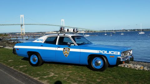 1991 Ford LTD Crown Victoria - Photograph of a vintage blue-and-white NYPD-style police sedan parked near a harbor with a bridge in the distance.