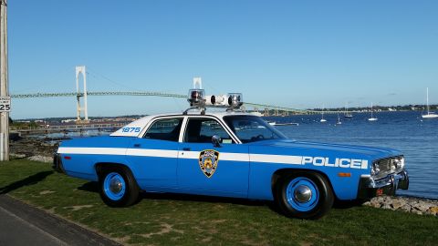 1991 Ford LTD Crown Victoria - Photograph of a restored blue-and-white police sedan parked by a harbor with a suspension bridge behind.