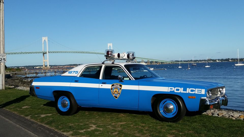 Blue and white vintage police sedan with roof lights at a waterfront