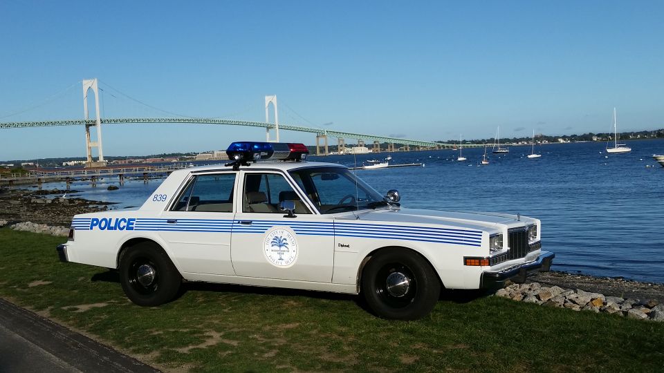 White and blue striped classic police sedan parked on grass by the water