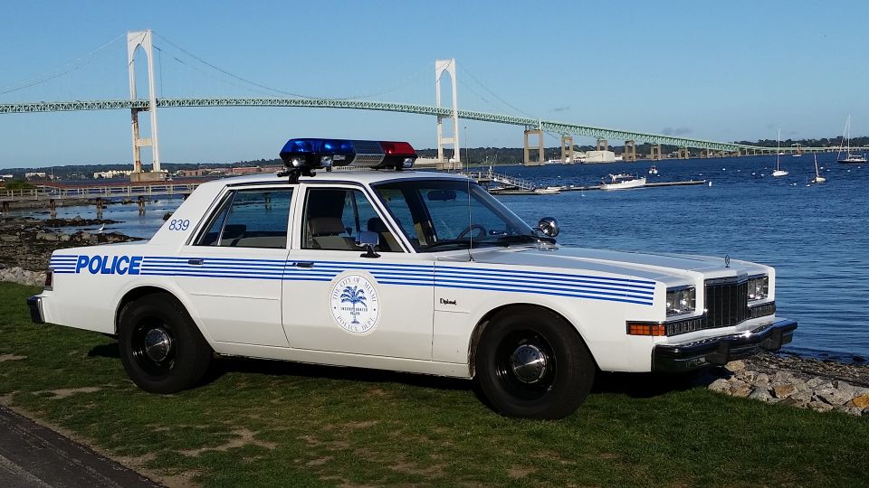 White and blue classic police sedan parked beside a harbor