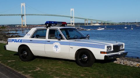 1991 Ford LTD Crown Victoria - Photograph of a vintage white-and-blue police sedan parked at a harbor with a suspension bridge behind.