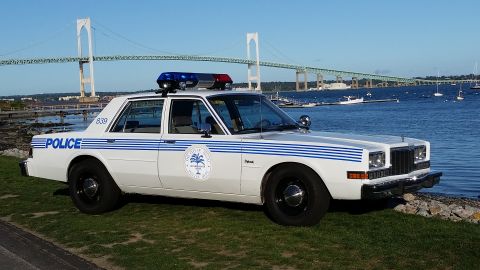 1991 Ford LTD Crown Victoria - Photograph of a vintage white-and-blue police sedan parked near a waterfront with a bridge in the background.