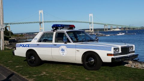 1991 Ford LTD Crown Victoria - Photograph of a vintage white-and-blue police sedan parked near a waterfront with a suspension bridge.