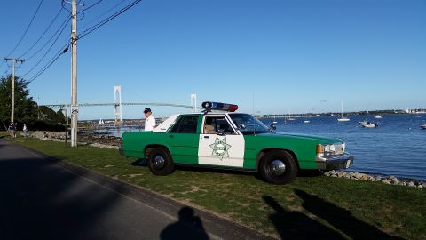1991 Ford LTD Crown Victoria - Photograph of a green-and-white vintage sheriff sedan parked along a road by a harbor with a bridge behind.