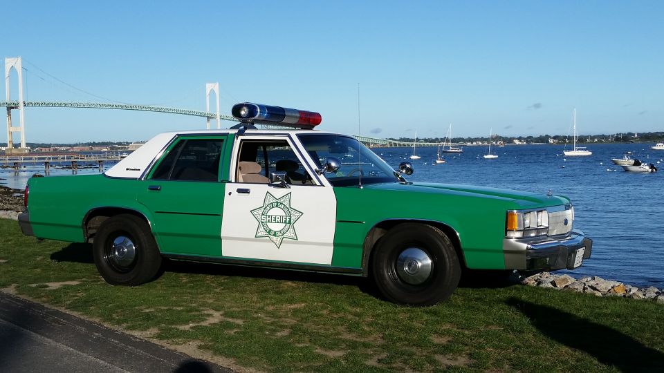 Green and white classic sheriff sedan with a star emblem by the harbor