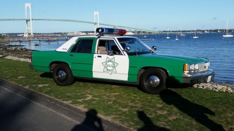 1991 Ford LTD Crown Victoria - Photograph of a vintage green-and-white sheriff sedan parked near a harbor with a suspension bridge behind.