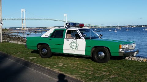1991 Ford LTD Crown Victoria - Photograph of a green-and-white sheriff sedan parked beside a waterfront with a suspension bridge in the background.