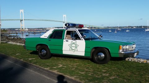1991 Ford LTD Crown Victoria - Photograph of a vintage green-and-white sheriff sedan parked at a harbor with a suspension bridge behind.