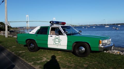 1991 Ford LTD Crown Victoria - Photograph of a green-and-white sheriff sedan parked near a harbor with a suspension bridge in the background.