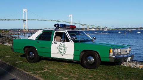 1991 Ford LTD Crown Victoria - Photograph of a vintage green-and-white sheriff sedan parked at a waterfront with a suspension bridge behind.