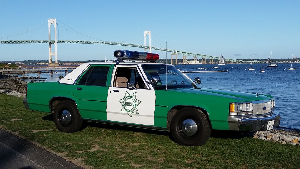 Green and white sheriff sedan parked on grass beside the harbor