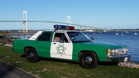 1991 Ford LTD Crown Victoria - Photograph of a green-and-white sheriff sedan with a star emblem parked near a harbor and suspension bridge.