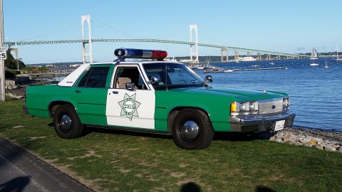1991 Ford LTD Crown Victoria - Photograph of a vintage green-and-white sheriff sedan parked at a waterfront with a suspension bridge in the background.