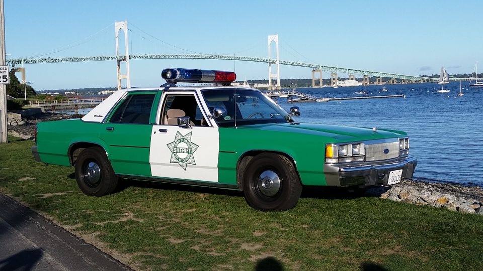 Green and white sheriff sedan with roof lights parked by the harbor