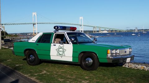 1991 Ford LTD Crown Victoria - Photo of a green-and-white sheriff Ford Crown Victoria police car parked beside a bay with a suspension bridge in the background.