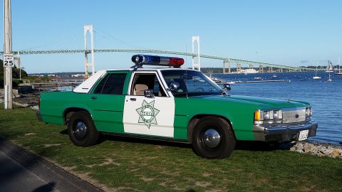 1991 Ford LTD Crown Victoria - Photo of a green-and-white sheriff Ford LTD Crown Victoria parked by the waterfront with a 25 mph speed sign.