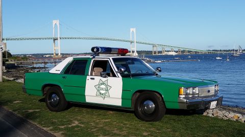 1991 Ford LTD Crown Victoria - Photo of a green-and-white sheriff Ford Crown Victoria parked on grass beside a bay and bridge.