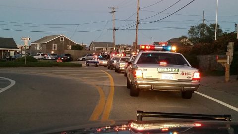 1991 Ford LTD Crown Victoria - Photo of a procession of police cruisers with emergency lights on, led by a sheriff Crown Victoria, on a coastal road at dusk.