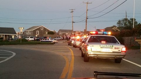 1991 Ford LTD Crown Victoria - Photo of a line of police cruisers with emergency lights led by a sheriff car on a seaside road at dusk.