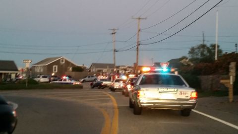 1991 Ford LTD Crown Victoria - Photo of police cruisers with flashing lights driving along a curving seaside road at dusk.