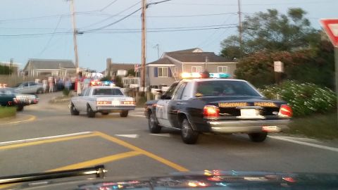 1991 Ford LTD Crown Victoria - Photo of a Highway Patrol Crown Victoria and other police cars with lights on along a seaside road at dusk.